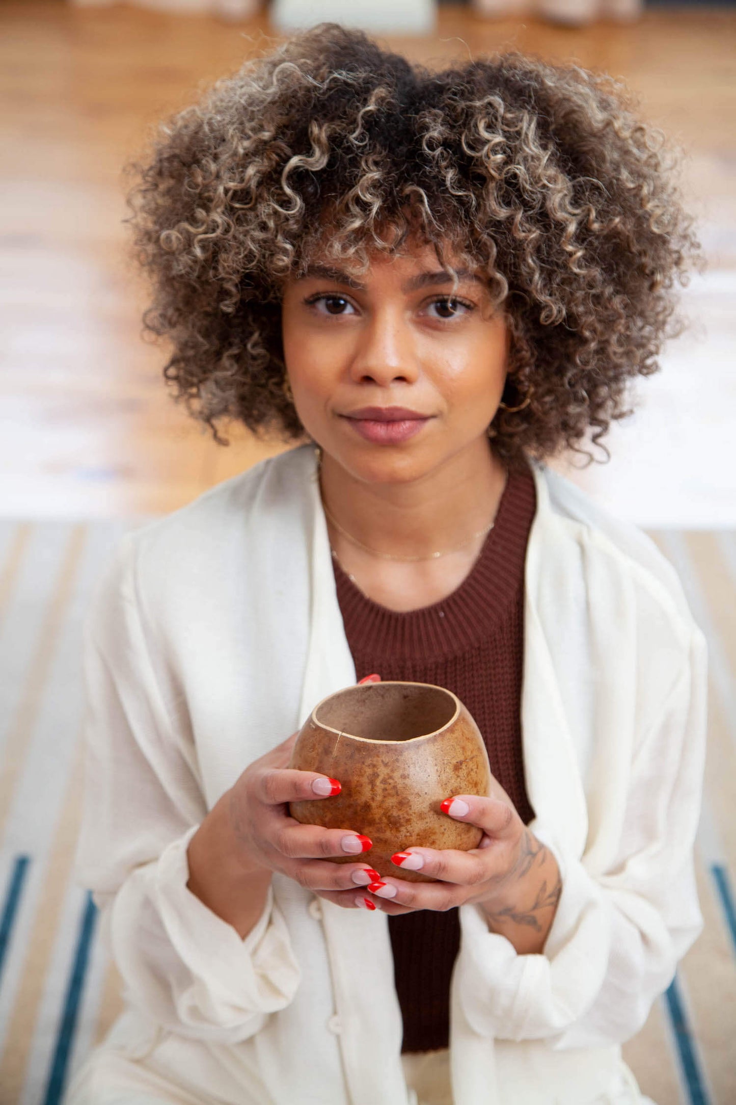 woman with curly hair holding a ceremonial gourd vessel